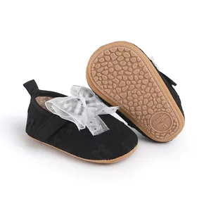 Detailed view of black baby prewalker shoes with a large white lace bow and tan sole.