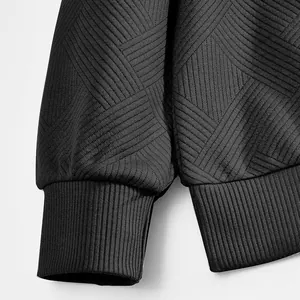 Détail macro d'une manche de sweat noir en jacquard avec poignets côtelés et texture