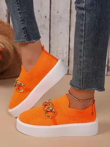 Detailaufnahme von orangefarbenen Fly-Knit-Sneakern mit Goldkette und Plateausohle