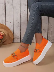 Nahaufnahme von orangefarbenen Strick-Plateauschuhen mit einer stilvollen Goldkettendekoration.