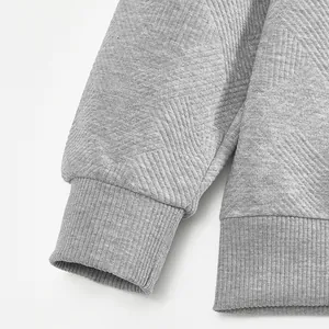 Gros plan sur la texture jacquard et les poignets côtelés du sweat-shirt gris