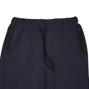 Detail view of dark blue men's joggers with elastic drawstring waist and zipper pockets.
