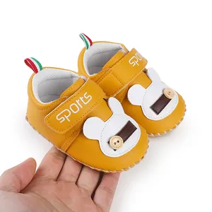 Dettaglio di scarpine gialle per neonati con design a coniglietto e chiusura a strappo.