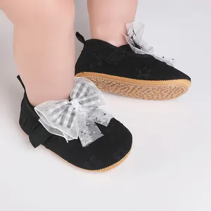 Close-up detail of black baby walker shoes with a large checkered bow and lace accents.
