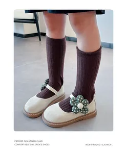 Nahaufnahme von cremefarbenen Mary Jane Kinderschuhen mit grüner Polka-Dot-Blume