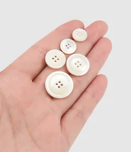 Close-up view of various sized cream-white mother of pearl shell buttons held in hand.