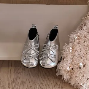 Macro view of silver metallic toddler boots with double bow details and side zipper