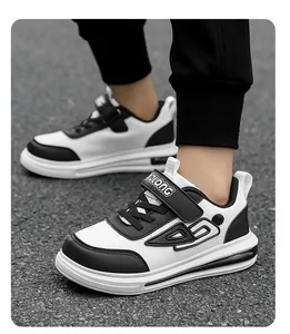 Stylish black and white children sneakers with velcro strap shown on asphalt ground