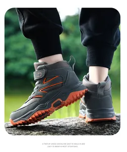 Side view of boys high-top outdoor hiking shoes with orange non-slip soles on a rock