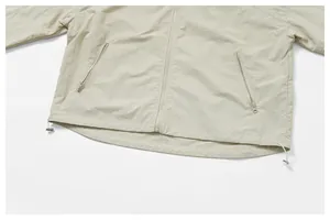 Detail view of a beige water-repellent windbreaker showing zippered pockets and adjustable hem.