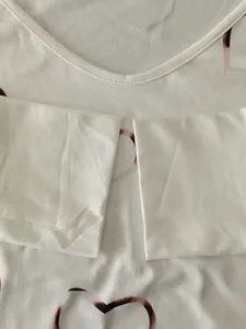 Close-up detail of white T-shirt showing collar, cuffs and red heart pattern print.
