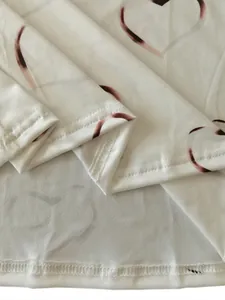 Close-up showing the high-quality hem stitching of a white heart-print long sleeve T-shirt.