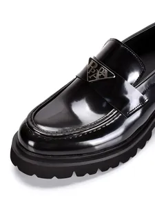 Close-up of black patent leather loafers with chunky soles and triangular metal plaque detail