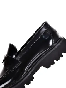 Close-up of black patent leather loafer showing metallic logo and thick lug sole.