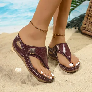 Detailed view of burgundy snakeskin texture on women's wedge flip-flops at beach sand