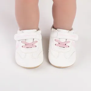 Nahaufnahme von weißen Baby-Lauflernschuhen mit rosa Schnürsenkeln und Klettverschluss.