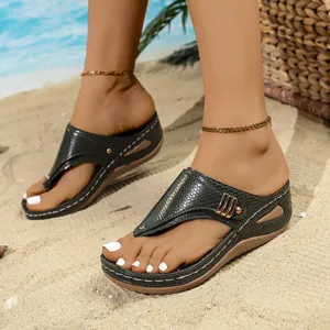 Detailed side view of dark green snake-pattern wedge flip-flops on the feet of a model on beach.