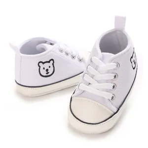 Λεπτομέρεια από λευκά βρεφικά πάνινα παπούτσια με κέντημα αρκουδάκι και μαλακή σόλα.