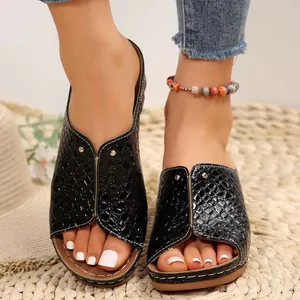 Primer plano de sandalias con cuña negras y grabado de cocodrilo con uñas blancas
