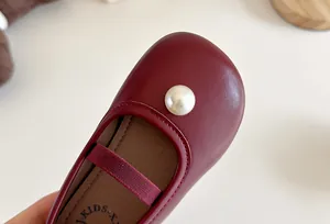 Close-up of burgundy girl's Mary Jane shoe with elegant pearl detail and round toe