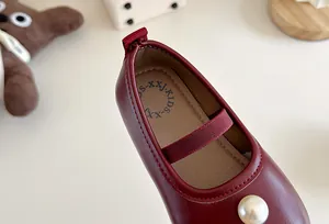Close-up of deep red girls' Mary Jane shoe with pearl detail and elastic strap.