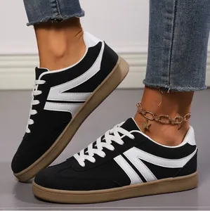Close-up detail of women's black and white retro lace-up flat sneakers worn with an anklet