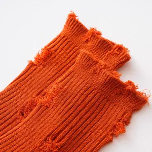 Close-up of bright orange kids' distressed ribbed crew socks with frayed holes design details.
