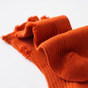 Detailed macro view of distressed orange ribbed kids mid-calf socks with ripped details.