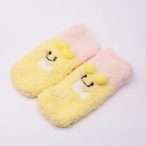 Soft plush baby socks with cute cartoon smiley faces and yellow pom-poms decoration.