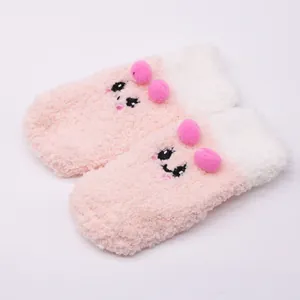 Close-up view of soft plush pink baby socks with cute cartoon face and pom-poms