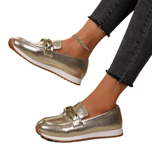 Glänzende goldene Loafer mit Kettendetails und weißer Sohle an Modelbeinen gezeigt.