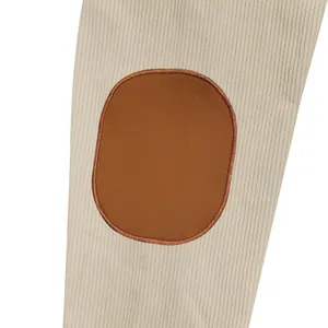 Macro close-up detail of a brown oval elbow patch on a ribbed beige corduroy jacket