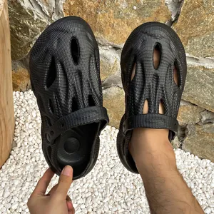 Detail von schwarzen Unisex-Outdoor-Clogs mit Netzstruktur auf weißen Kieselsteinen.