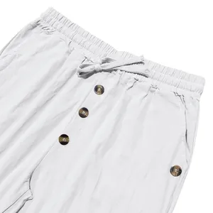 Close-up of white men's casual linen pants featuring drawstring elastic waist and brown buttons.