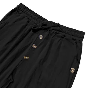 Detail view of black linen trousers with elastic drawstring waist and decorative buttons.