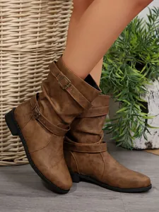 Detailed side view of brown slouchy mid-calf boots with decorative buckle straps on model