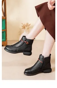 Close-up of black leather ankle boots with decorative brown strap and side zipper