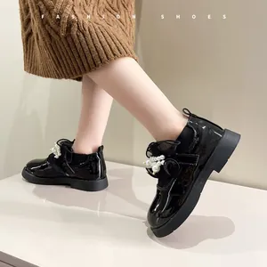 Close-up view of elegant girls' black patent leather shoes with pearl bow detail and sock cuff