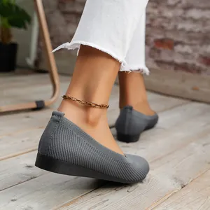 Close-up detail shot of women's grey breathable knit ballet flats worn on wooden floor.