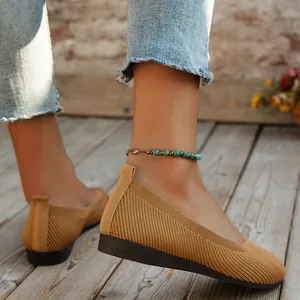 Detailed view of women's brown knitted round toe flat shoes worn on a wooden floor