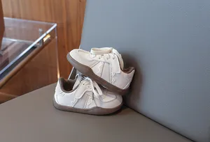 Weiße Kinder-Skateschuhe mit Spitzendetails und weichen braunen Sohlen auf Grau