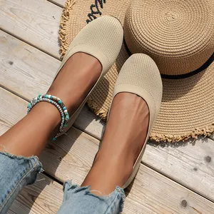 Close-up of breathable beige knit flat shoes worn on a wooden deck with a summer straw hat