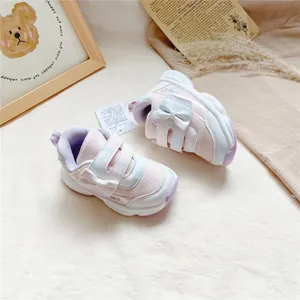 Gros plan de baskets roses pour filles avec un nœud blanc et une fermeture velcro.