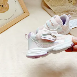 Détail de baskets roses pour petites filles avec nœud décoratif et fermeture velcro pratique.