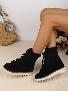 Gros plan de bottes de neige noires à lacets avec doublure en fourrure sur un tapis.