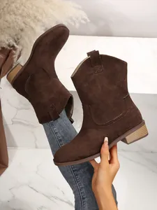 Detail view of dark brown suede Western cowboy boots with chunky heels and pointed toes.