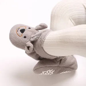 Gros plan sur des chaussons bébé ours gris portés avec un legging côtelé blanc