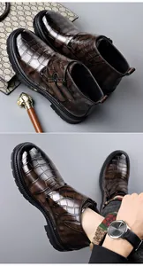Vista detallada de botas Chelsea marrones con grabado de cocodrilo, hebilla y acabado texturizado
