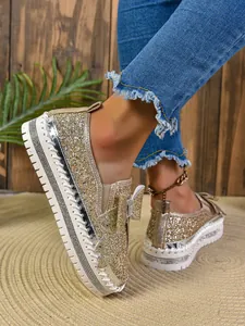 Close-up of women's gold glitter loafers featuring a sparkling bow and white sole.