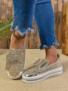 Close-up view of sparkly gold sequin flat shoes featuring a large bow and rhinestone accent